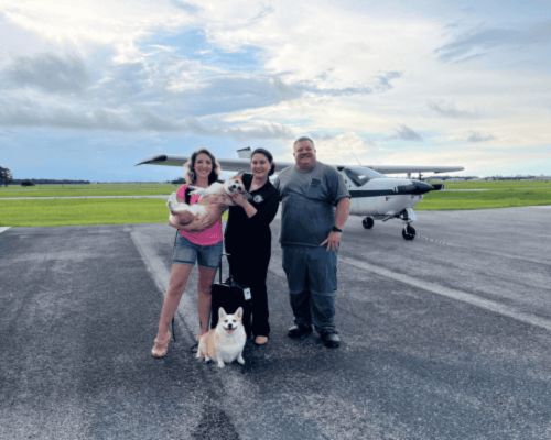 Pet owners and a Professional Pets Florida team member with two dogs in front of a small plane